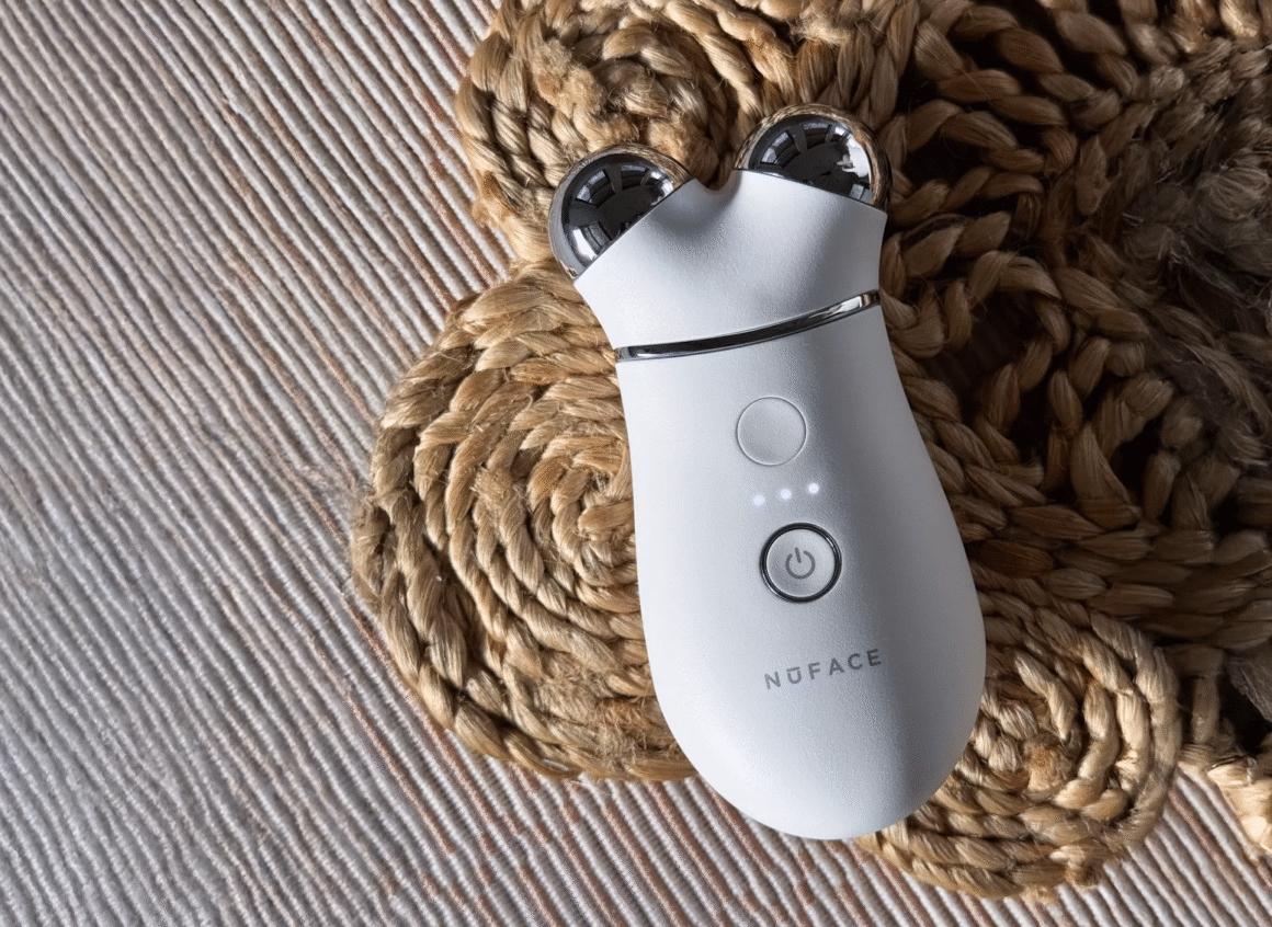 Close-up of the NuFACE Trinity microcurrent device placed on a textured woven surface, showing its power button and dual silver spheres.