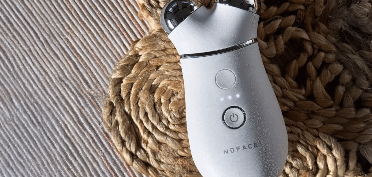 Close-up of the NuFACE Trinity microcurrent device placed on a textured woven surface, showing its power button and dual silver spheres.