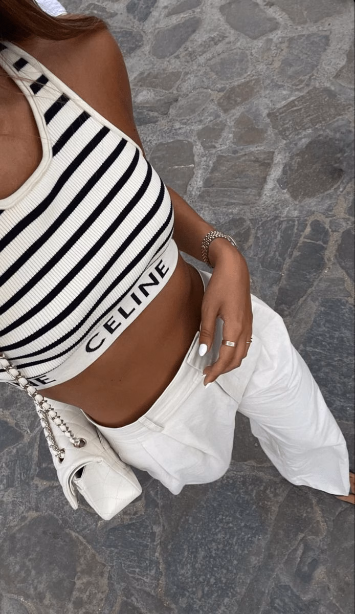 Woman wearing a black-and-white Celine striped halter top with tailored white pants and a quilted shoulder bag